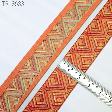 two pieces of fabric with a geometric pattern in shades of orange and red, placed next to a ruler for size comparison.