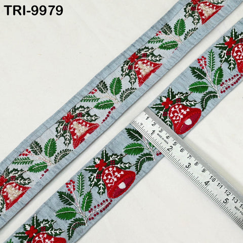 a decorative fabric with a repeating pattern of red and green leaves and bells, and a ruler placed next to it to measure the length of the fabric.