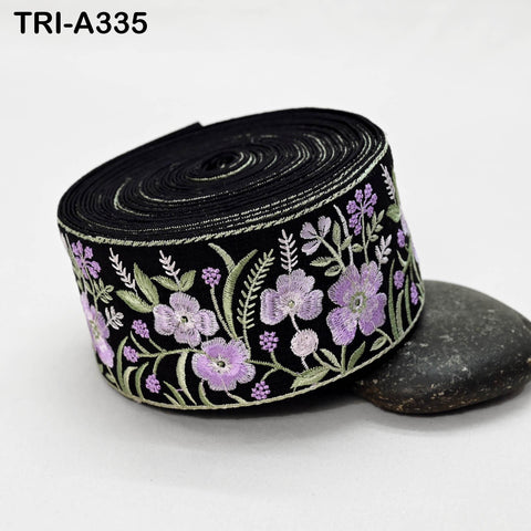 A black fabric with a floral embroidered design in shades of purple and green.