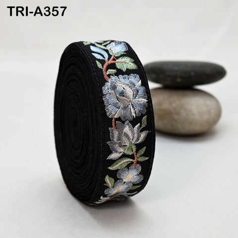 A black, circular spool of thread with a floral embroidered design on it, placed on a white surface.