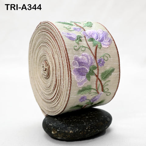A roll of fabric with a floral pattern, featuring purple flowers and green leaves, is displayed on a black rock.