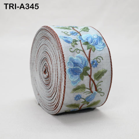 A roll of embroidered fabric with a floral pattern, featuring blue flowers and green leaves.