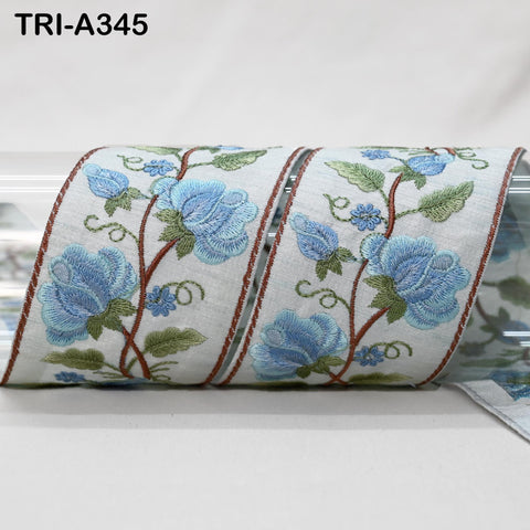 a decorative fabric with a floral pattern, featuring blue flowers and green leaves. The fabric appears to be a decorative trim or ribbon, with a repeating pattern of blue flowers and green leaves.