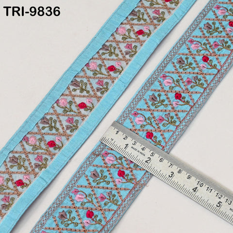 two pieces of blue fabric with intricate floral embroidery, and a ruler is placed on top of the fabric to measure its length.