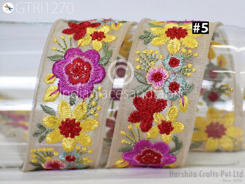 a decorative fabric with a floral pattern, including red, yellow, and purple flowers, as well as green leaves. The fabric appears to be a beige or light-colored material, possibly a ribbon or a piece of clothing.