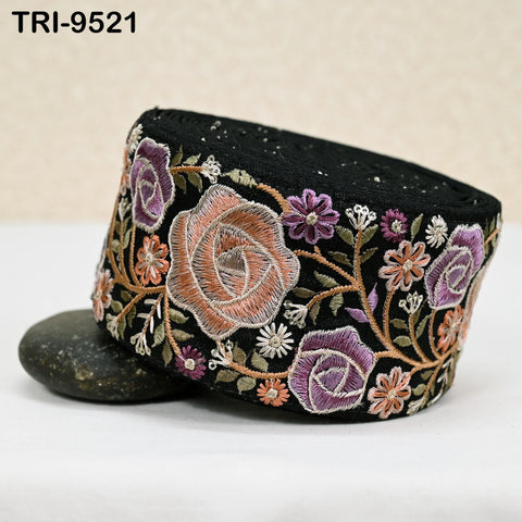 a decorative black fabric with a floral pattern, including roses and other colorful flowers. The fabric is placed on a white surface, and there is a small black rock in the foreground.