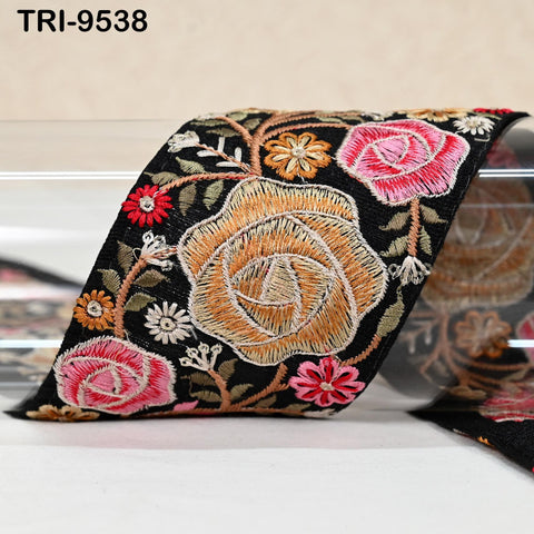 a close-up view of a decorative fabric with a floral pattern, including roses and other colorful flowers. The fabric appears to be black with a vibrant, intricate embroidered design.