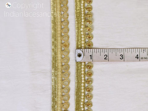 two gold-colored decorative trim pieces, with a ruler placed between them to measure their length.