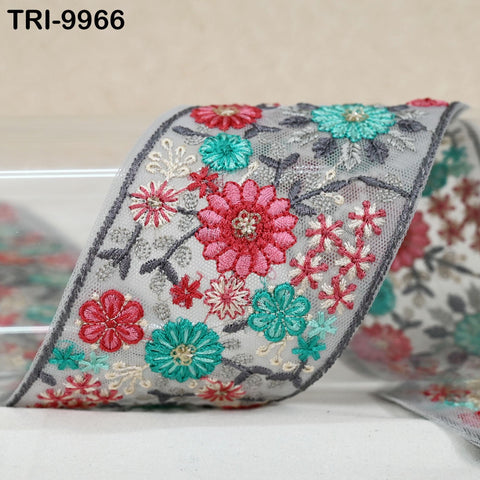a close-up view of a decorative fabric with a floral pattern. The fabric is adorned with a variety of colorful flowers, including red, green, and white ones, arranged in a visually appealing manner. The fabric appears to be a piece of lace or a similar type of textile, with intricate embroidery work visible on its surface.