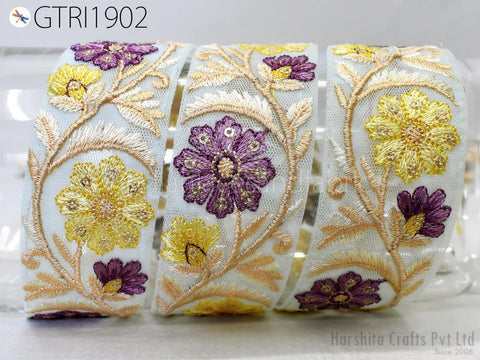 a close-up view of a decorative fabric with a floral pattern. The fabric is adorned with yellow and purple flowers, and the design is intricate and detailed. The fabric appears to be a piece of embroidered lace or a similar type of textile.