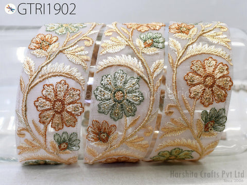 a close-up view of a decorative fabric with a floral pattern. The fabric is adorned with multiple green and orange flowers, as well as leaves, creating a visually appealing and intricate design. The fabric appears to be rolled up and displayed, possibly for sale or as a decorative piece.