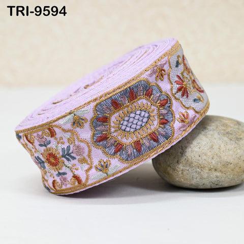 A decorative fabric with a floral pattern and a metallic border is displayed on a white surface, with a rock placed next to it.