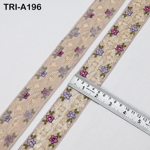 a close-up view of a decorative ribbon with a floral pattern. The ribbon is placed on a white surface, and a ruler is visible, indicating its size.