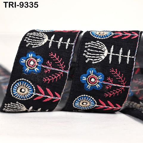 two pieces of black fabric with intricate floral embroidery designs in various colors, including blue, red, and white.