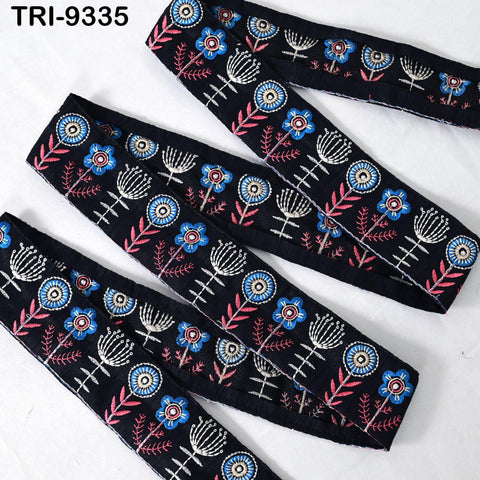 a collection of black fabric pieces with intricate floral embroidery patterns in shades of blue, pink, and white. The pieces appear to be part of a larger collection or product line, as indicated by the text "TRI-935" in the top left corner.
