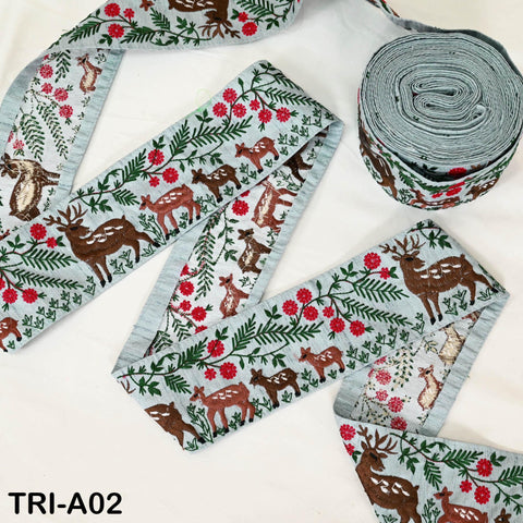 a collection of decorative fabric pieces featuring a repeating pattern of deer and floral elements. The fabric appears to be a type of ribbon or textile, with a light blue color and a floral design. The image also includes a spool of the same fabric, suggesting it is being used for a crafting or sewing project.