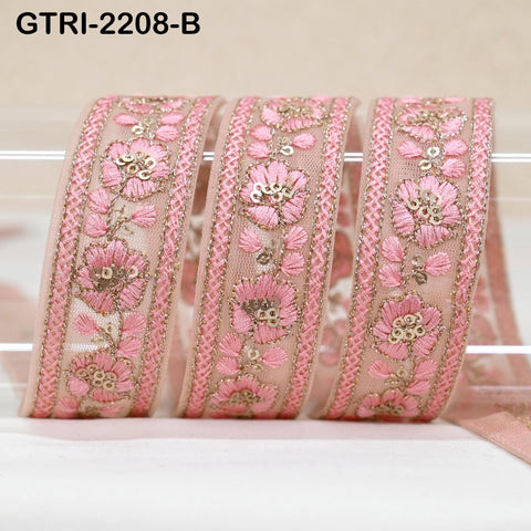 A close-up image of a decorative pink fabric ribbon with intricate floral embroidery.