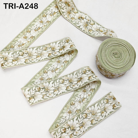 a roll of green and white floral embroidered fabric, with a spool of the same material visible next to it.