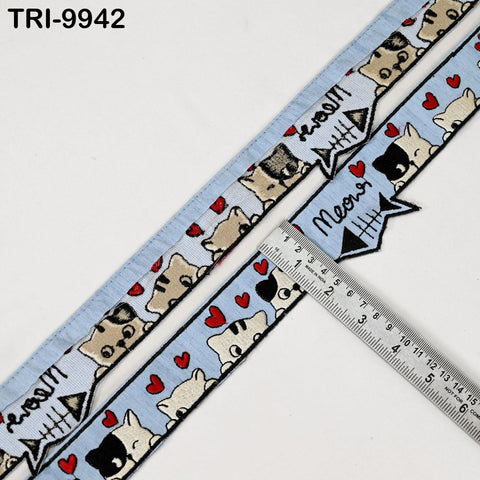 a blue ribbon with a repeating pattern of cartoon cat faces and hearts. The ribbon is laid out on a white surface, and a ruler is placed next to it, indicating the ribbon's length.