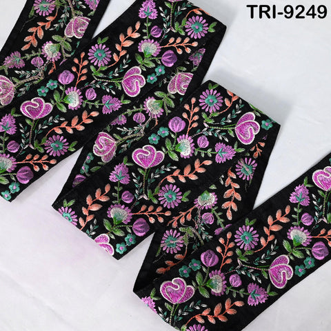 a close-up view of a decorative fabric with a floral pattern in shades of purple, pink, and green. The fabric appears to be black, and the pattern features various flowers and leaves. The fabric is arranged in a zigzag pattern, creating a visually appealing and intricate design.