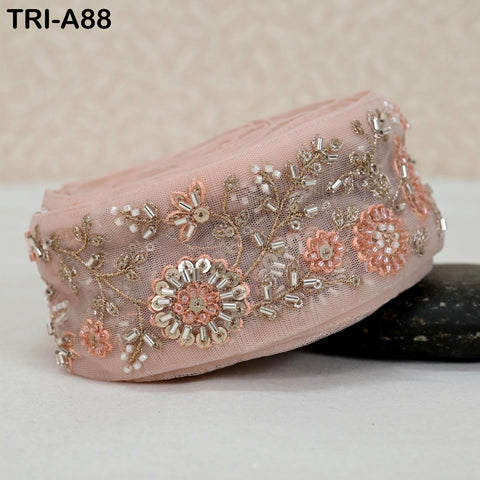 A pink fabric with intricate floral embroidery and beading, including small flowers and leaves, is displayed on a surface.
