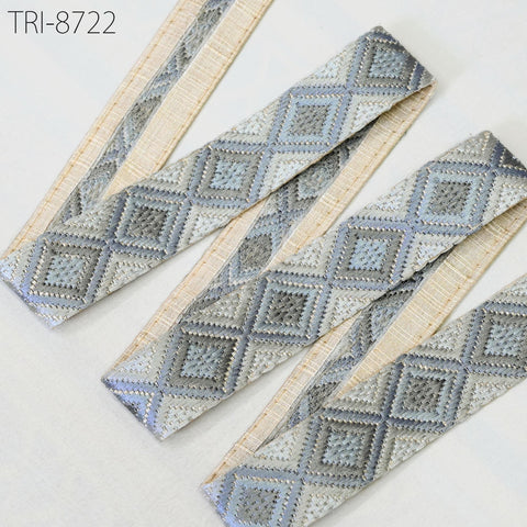 a close-up view of a decorative fabric with a diamond pattern in shades of gray and beige. The fabric appears to be made of a material with a textured, woven appearance.