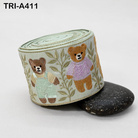 A decorative fabric with embroidered teddy bears wearing overalls, sitting on a black rock.