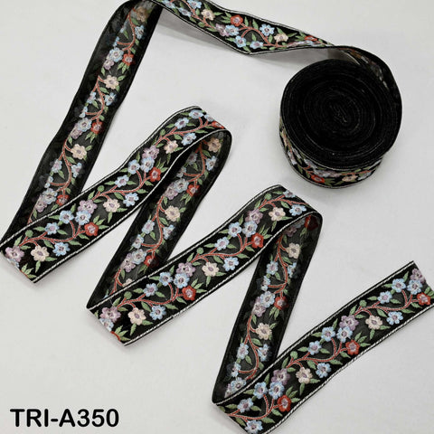 a spool of black and white embroidered ribbon with a floral pattern, and a smaller spool of the same ribbon with a different floral pattern.
