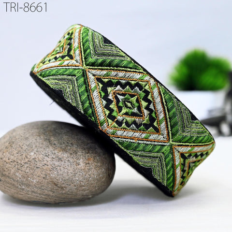 a decorative green and black patterned object, possibly a piece of jewelry or a headband, placed on a gray rock.