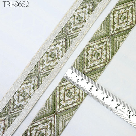 a close-up view of a decorative fabric with a repeating pattern of diamond shapes in shades of green and white. The fabric appears to be a decorative trim or border, and a ruler is placed next to it to measure its length.