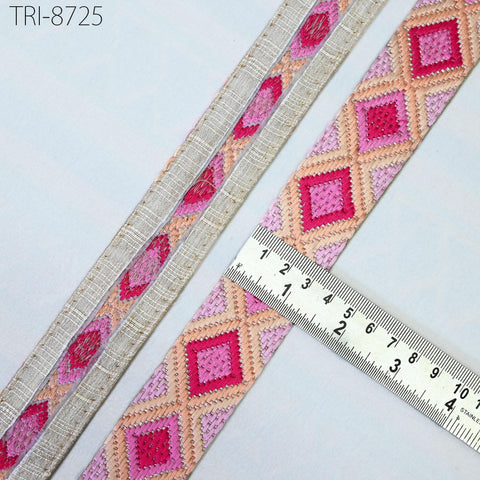 a close-up view of a decorative fabric with a repeating pattern of pink and orange diamond shapes. A ruler is placed next to the fabric, indicating its size or length.