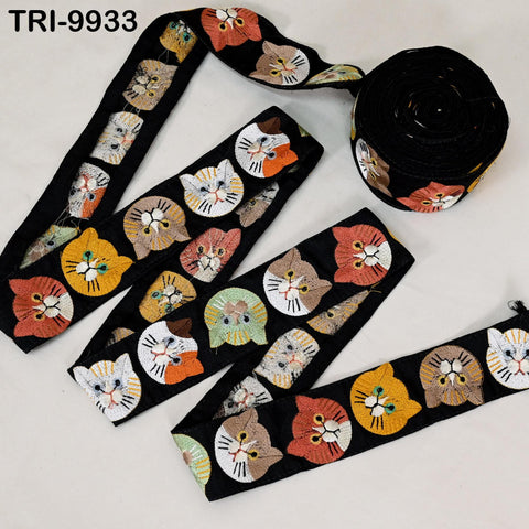 a collection of cat-themed fabric pieces, including a spool of black fabric with a repeating pattern of cat faces in various colors and sizes, as well as several individual pieces of fabric with the same cat face designs.