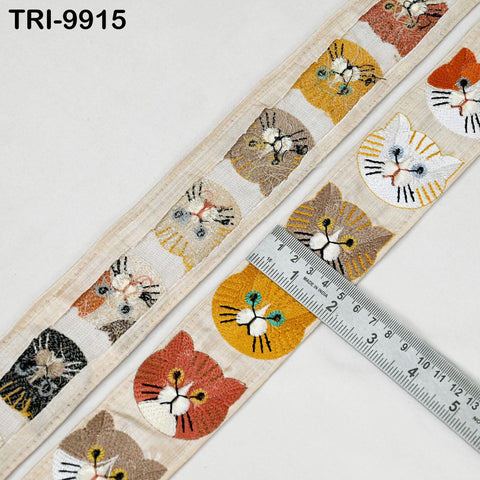a beige fabric with a repeating pattern of cat faces, including various shades of brown, orange, and white. A ruler is placed on the fabric, likely for measuring the size or dimensions of the pattern.