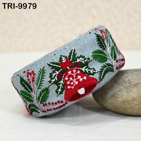 A decorative fabric with a red bell and holly leaves design, placed on a white surface next to a rock.