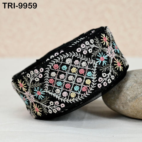 a black, intricately embroidered piece of fabric with a floral pattern, resting on a surface with a rock.